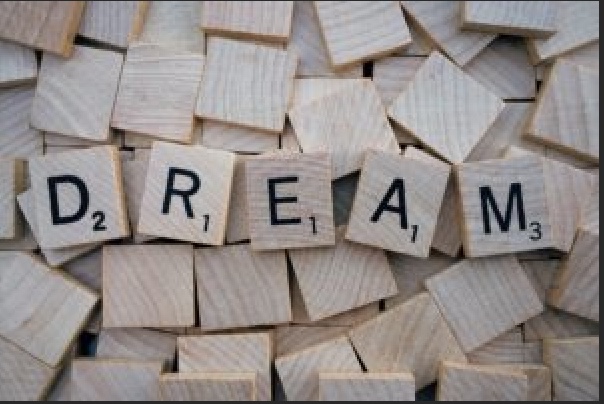 Słowo 'Dream' ułożone z liter Scrabble na tle wielu rozsypanych kostek – metafora marzeń, nadziei i kreatywności.